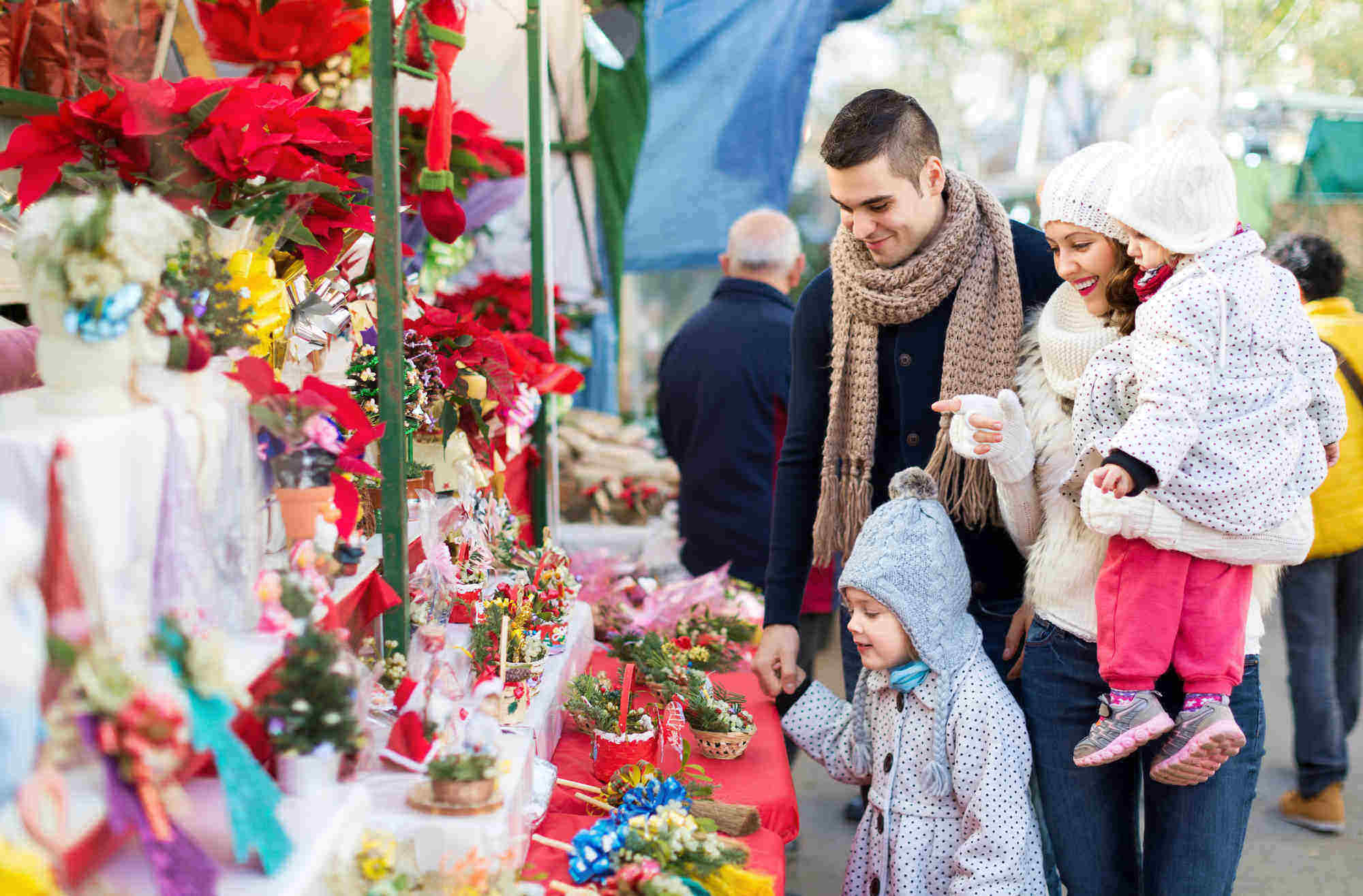 Smiling parents and little children buying red Euphorbia at Christmas fair. Focus on woman